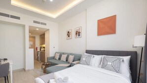 Una habitación de hotel moderna con una cama, un sofá, una mesita y una kitchenette al fondo.