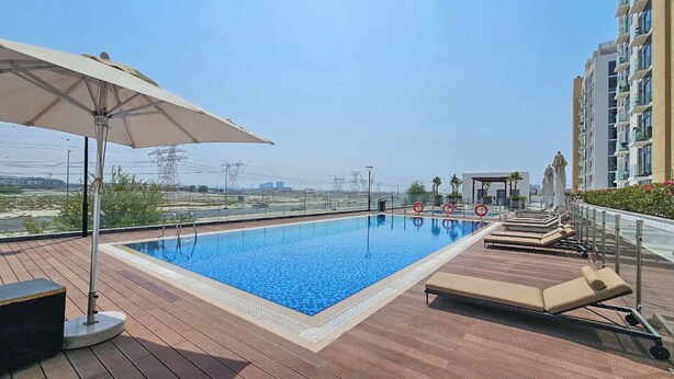 Una piscina en la azotea con sillas de descanso y una sombrilla, rodeada por un edificio de gran altura.
