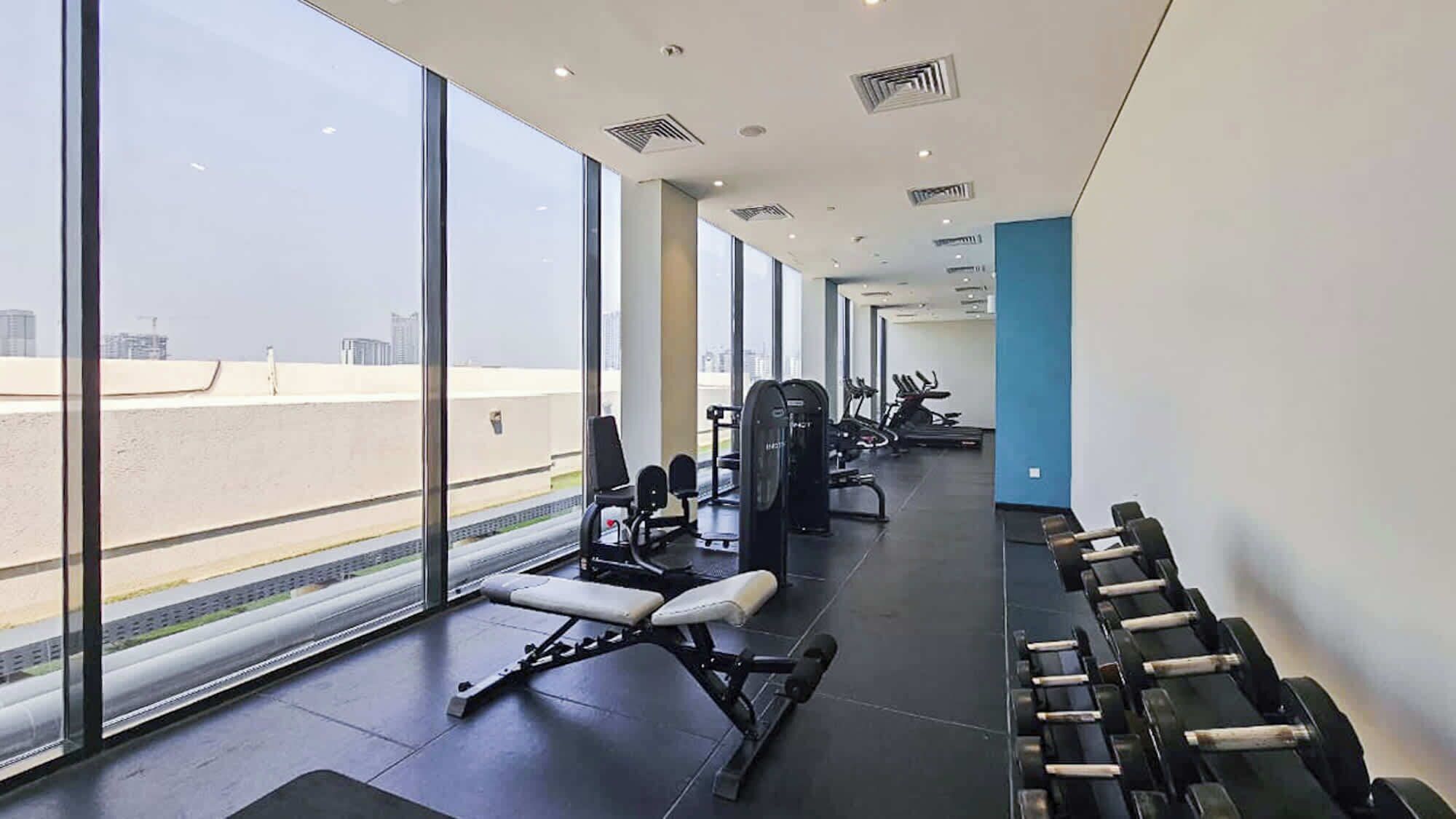 Ein Fitnessstudio mit Trainingsgeräten, großen Fenstern und Blick auf die Stadtlandschaft.