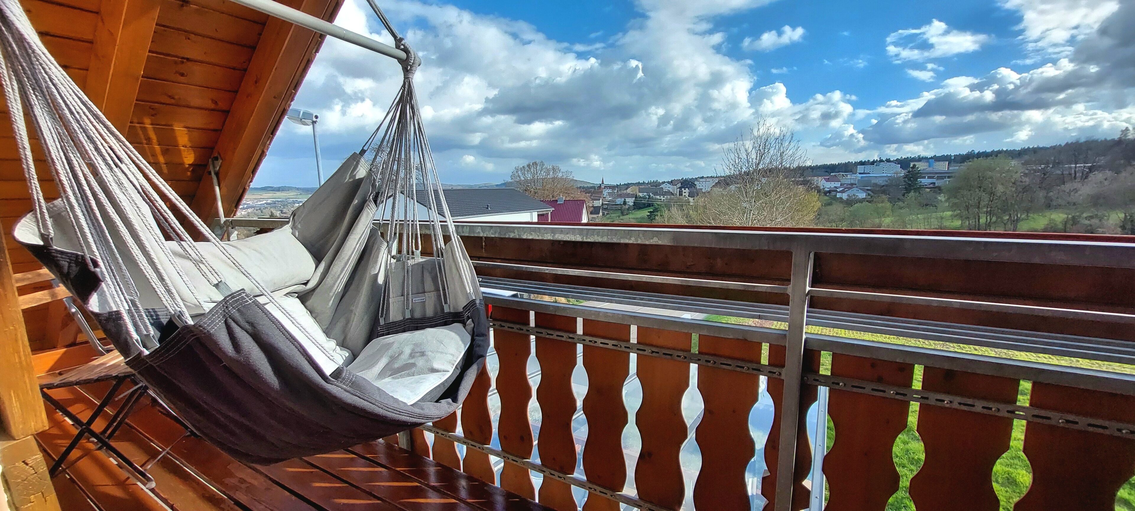 A hammock chair on a balcony with a view of a town and hills.