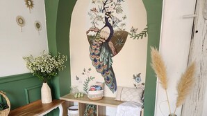 A room with a green wall, a wooden bench, a shelf with books and decorative items, a hanging light fixture, and a vase with pampas grass.