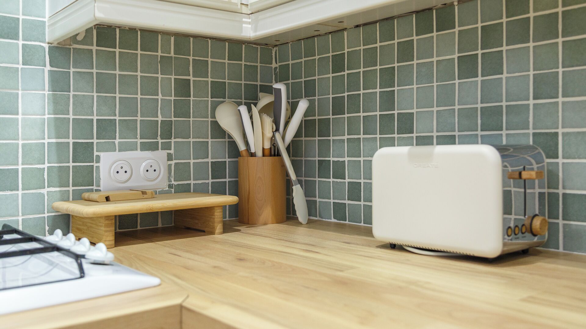 A compact kitchen with a wooden countertop, a toaster, a knife block, and a power strip.