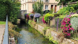 Un canal con un muro de piedra a un lado y una barandilla de metal al otro. Hay flores y plantas coloridas a lo largo de la barandilla.