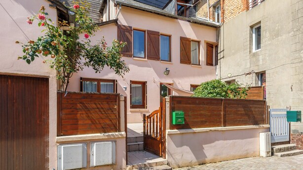 Un edificio de dos pisos con un portón de madera, una pequeña escalera y un buzón verde.