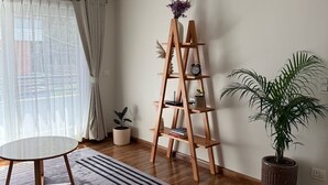 Een kamer met een houten laddenplank, een ronde tafel, een potplant en een raam met gordijnen.