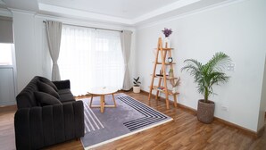 Een woonkamer met een donkere bank, een houten ladder, een potplant en een gestreept vloerkleed.