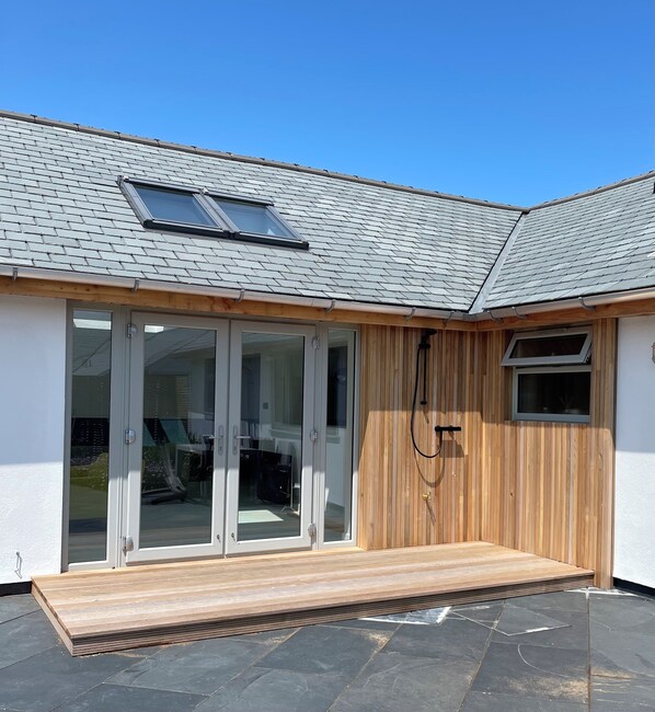 A modern house with a sloped roof, large sliding glass doors, a wooden deck, and a small window.