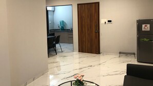 Una sala de estar moderna con suelo de mármol, una puerta de madera, un refrigerador y un comedor con mesa y sillas.