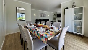 A dining area with a table set for four, chairs, a cabinet with glass doors, and a mirror on the wall. - ALBUFEIRA SUMMER VILLA 3 WITH POOL by HOMING (Albufeira)