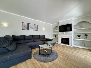 A modern living room with a sectional sofa, a round coffee table, a fireplace, and a mounted TV. - ALBUFEIRA SUMMER VILLA 3 WITH POOL by HOMING (Albufeira)