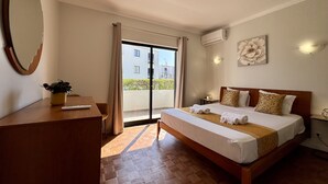 A hotel room with a bed, a desk, a mirror, a potted plant, and a view of the outside. - ALBUFEIRA SUMMER VILLA 3 WITH POOL by HOMING (Albufeira)