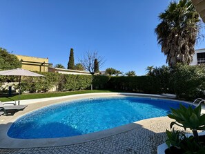 A swimming pool with a tiled edge, surrounded by a hedge and a palm tree. - ALBUFEIRA SUMMER VILLA 3 WITH POOL by HOMING (Albufeira)