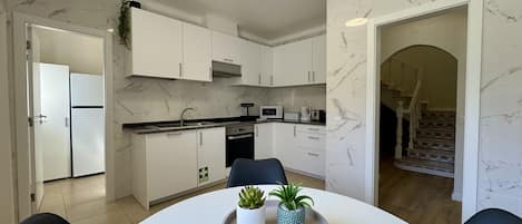 Cozinha moderna com armários brancos, micro-ondas embutido e área de refeições com mesa redonda e duas cadeiras.