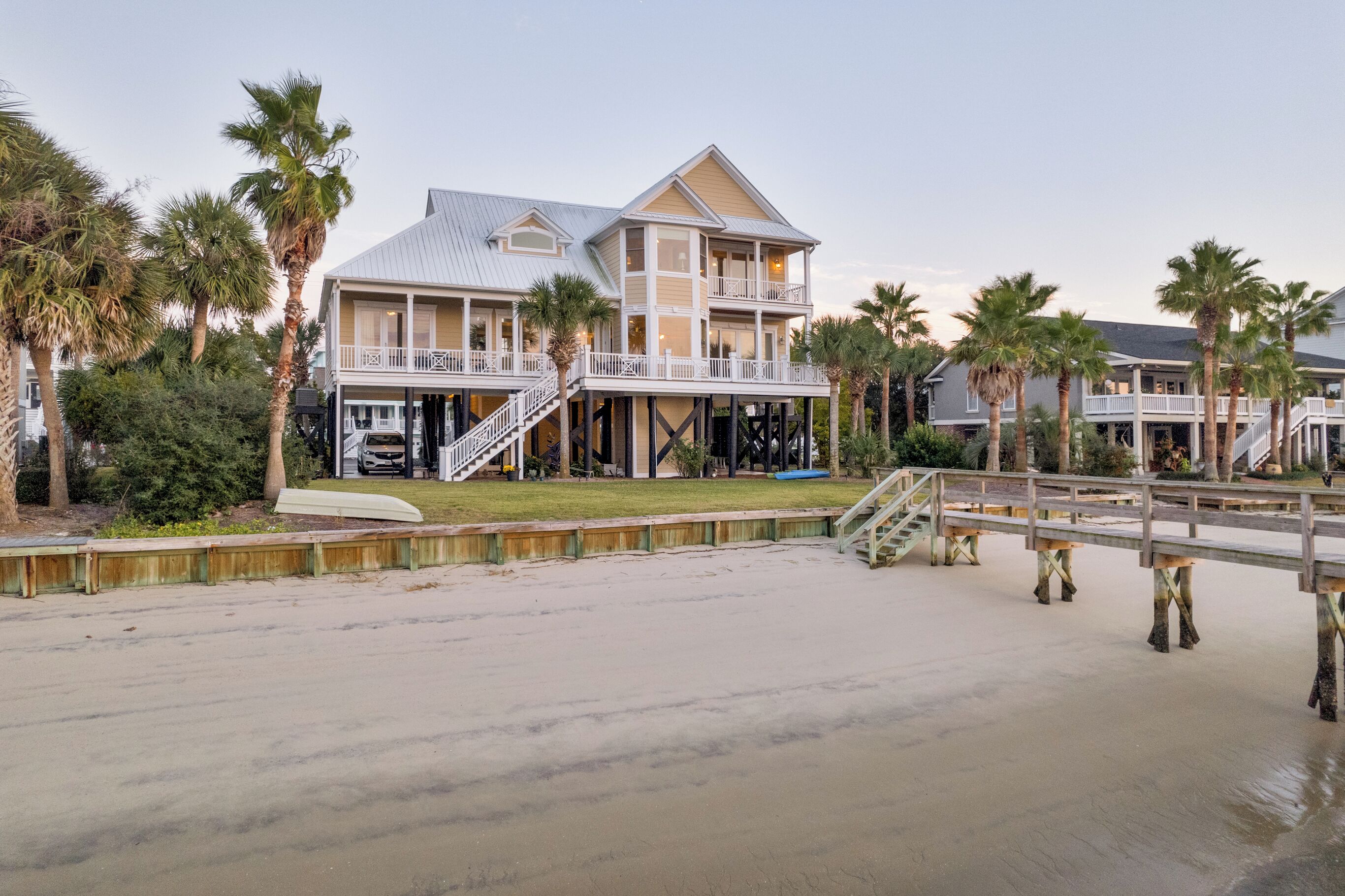 Een strandhuis met een twee verdiepingen, een overdekt terras en een houten looppad naar het strand.