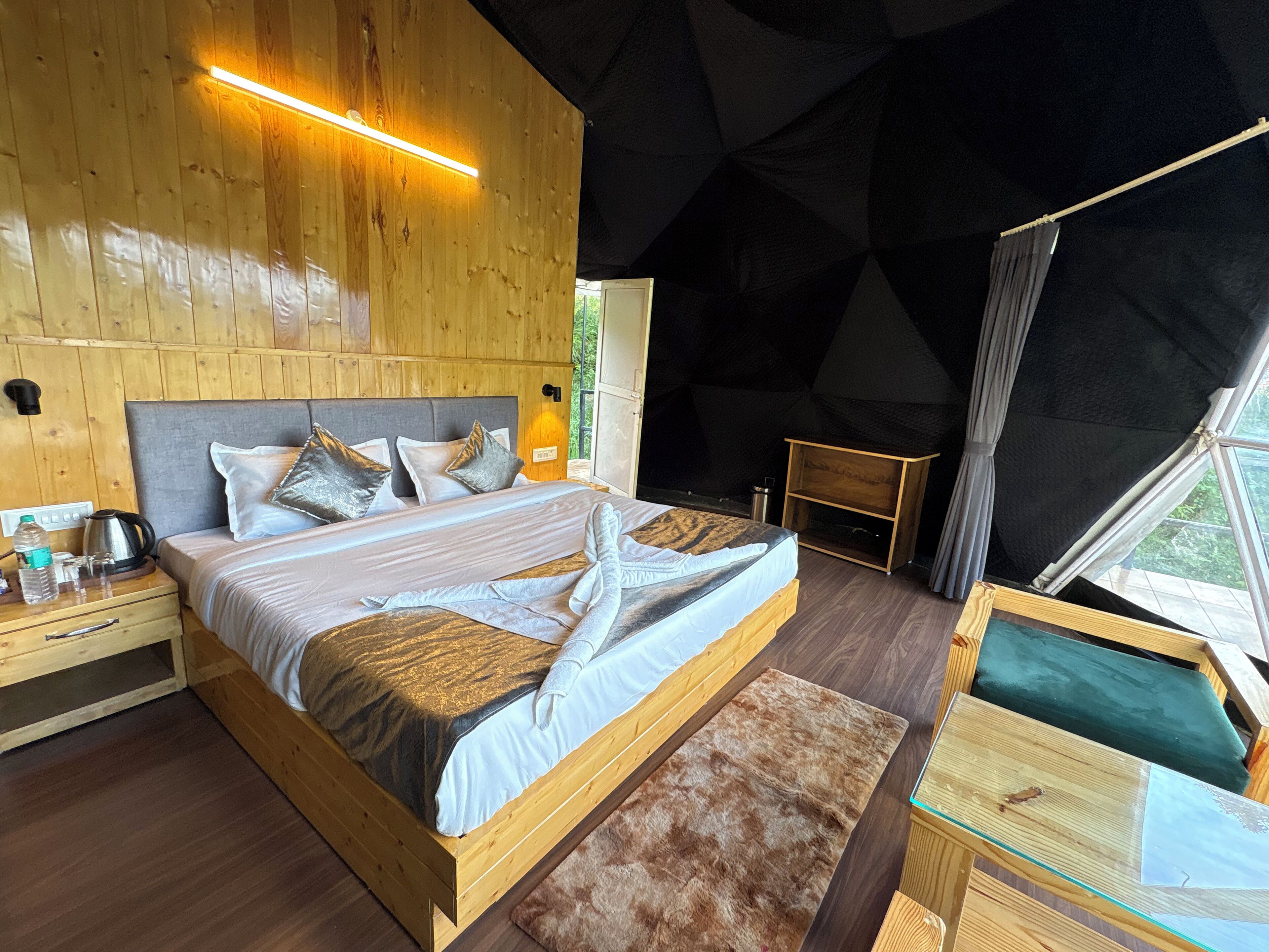 A wooden bedroom with a bed, bedside table, and a view of the outdoors.