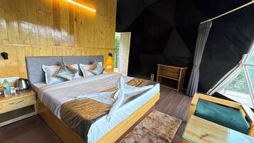 A wooden bedroom with a bed, bedside table, and a view of the outdoors.