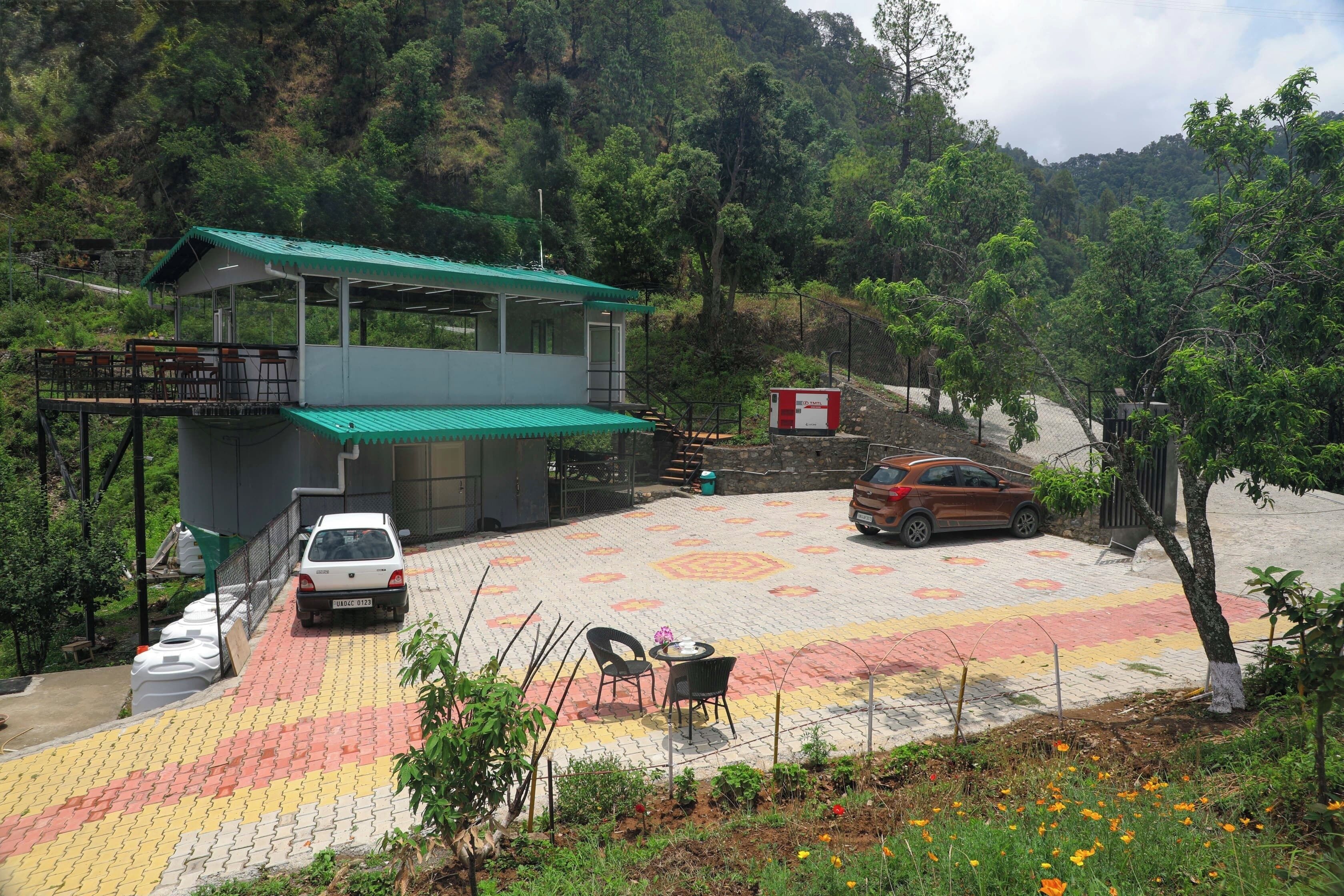 A building with a green roof and a covered outdoor area with a paved floor, surrounded by trees and a hillside.