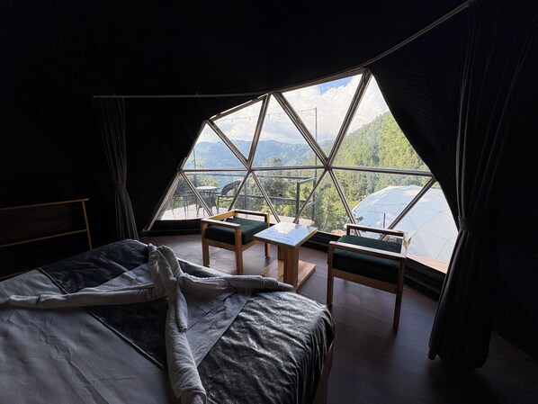 Una habitación con una cama, dos sillas, una mesita y vistas a montañas a través de un amplio ventanal.