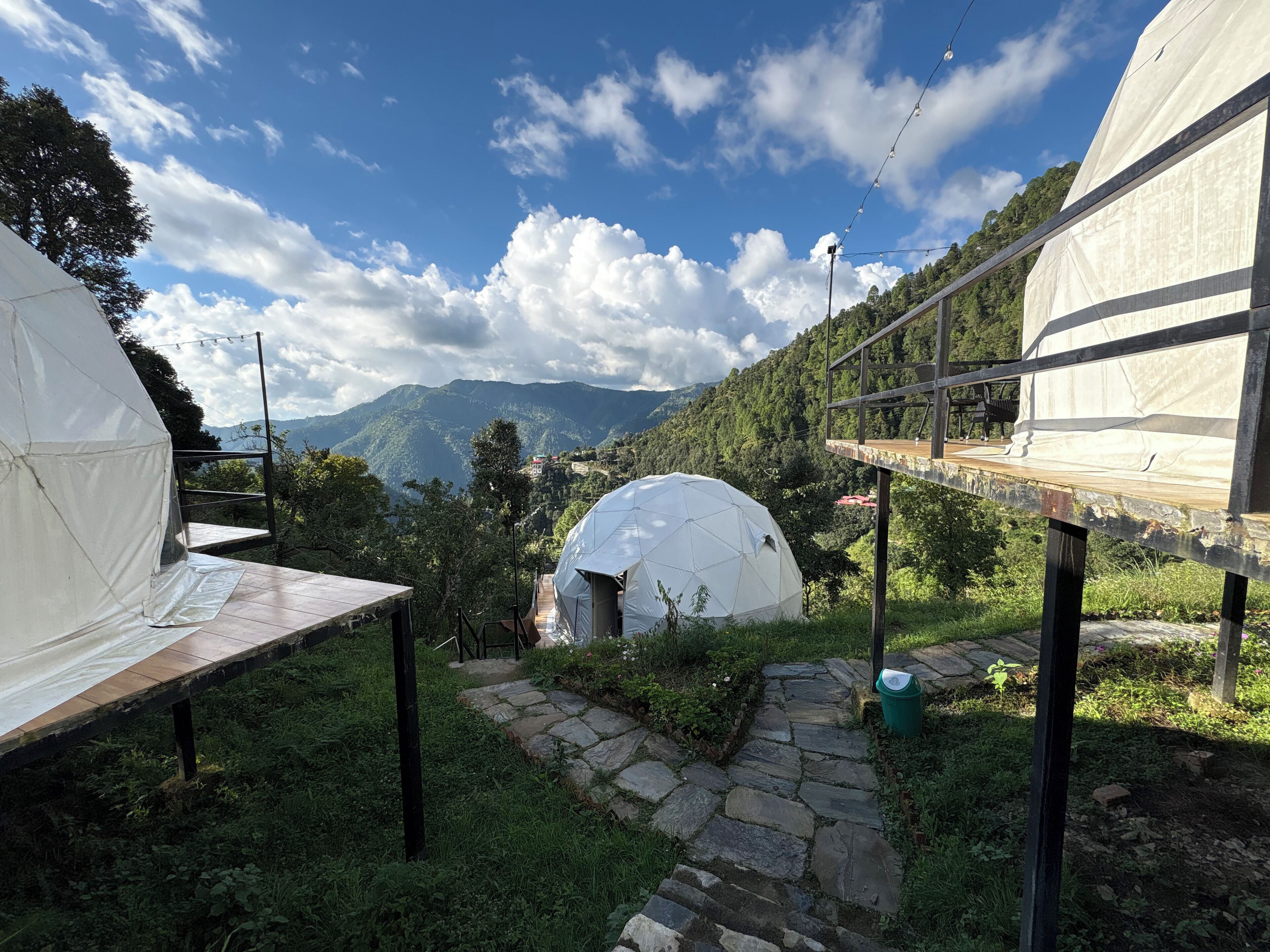 A dome-shaped tent with a stone pathway leading to it, surrounded by lush greenery and mountains in the background.