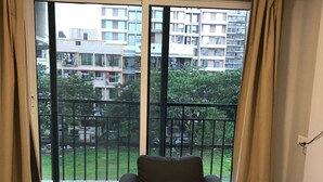 Ein modernes Wohnzimmer mit großem Fenster, einem schwarzen Sessel, einem Glastisch mit Blumenvase und einer weißen Klimaanlage.