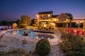 Una piscina con área de terraza, asientos exteriores y un porche cubierto con guirnaldas de luces.