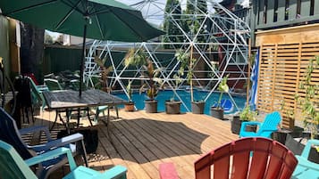 A wooden deck with outdoor furniture, a pool, and a geodesic structure.