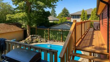 A backyard with a swimming pool, a barbecue grill, and a wooden deck.