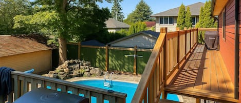 A backyard with a swimming pool, a barbecue grill, and a wooden deck.