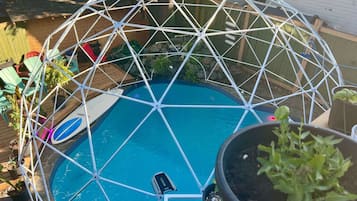 Een geodetische koepelstructuur boven een zwembad, met potplanten en tuinmeubilair.