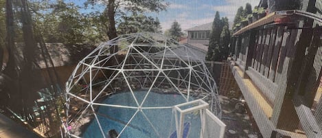 Vista a través de una ventana que muestra una estructura geométrica, posiblemente una escultura, y una piscina.