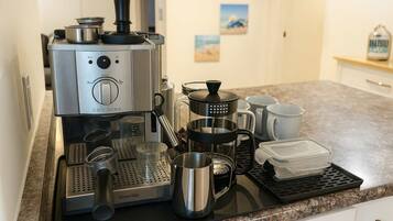 A kitchen with a Breville coffee maker, a coffee pot, a French press, and various coffee cups and containers.