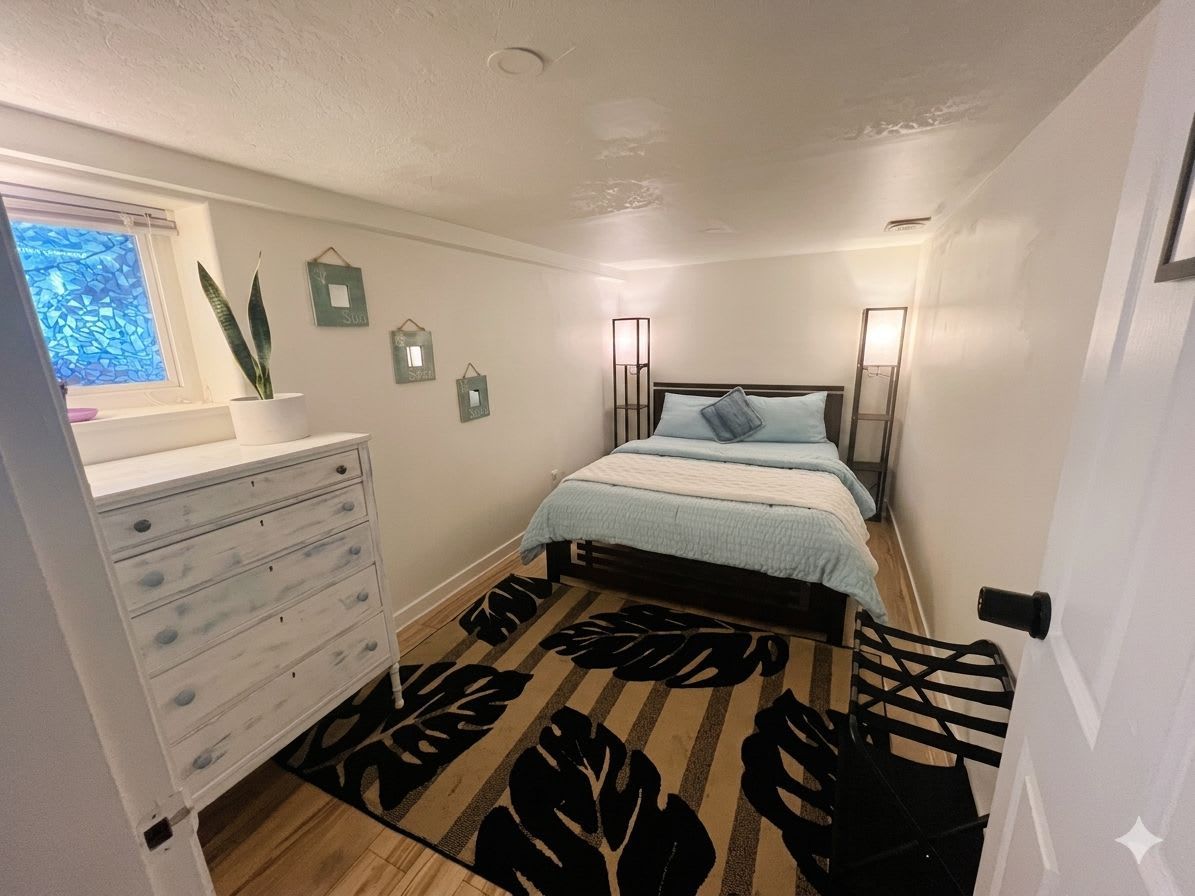 A bedroom with a bed, dresser, bedside lamps, and a window with a plant.
