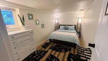 A bedroom with a bed, dresser, bedside lamps, and a window with a plant.