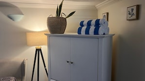 A white cabinet with a plant and towels on top, a lamp, and a framed picture on the wall. - Poolside Hideaway • Heated Pool All Year • Ideal for Groups (Sleeps 6+) (Victoria)