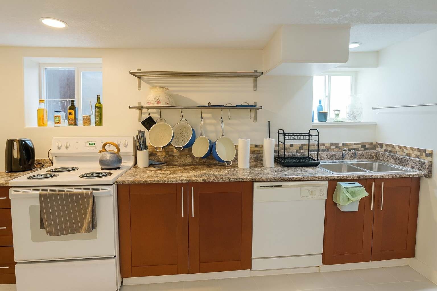 Una cucina moderna con piano cottura, forno e lavastoviglie, una finestra con bottiglie e un ripiano con pentole e padelle.