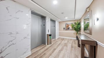 A hallway with marble flooring, two elevators, a recycling bin, and a wooden bench.