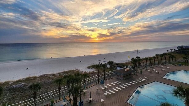 A beach view with a sunset, a pool area, and a fenced walkway. - Sunny Daze 104-Walk-Out Beachfront-Sleeps 6 (Panama City Beach)
