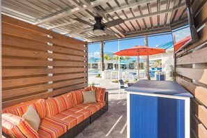A covered outdoor seating area with a pool view, a bar, and a ceiling fan.