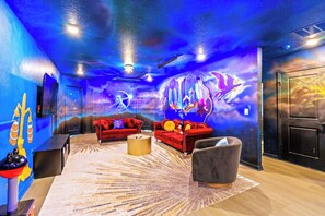 Quarto com mural estrelado, sofás vermelhos, uma mesa de centro redonda e uma porta preta.