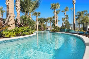 A swimming pool with a curved edge, surrounded by palm trees and other tropical plants.