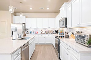 A modern kitchen with white cabinetry, stainless steel appliances, and a marble countertop. - New Resort, Private Pool & Spa, Outdoor Theater, Game Room, Minutes to Disney World (Clermont)