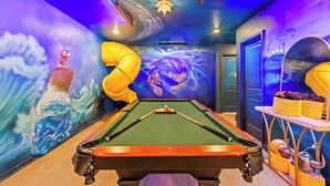 A pool table with a green felt surface, surrounded by walls with a mural of a wave and a starry sky.