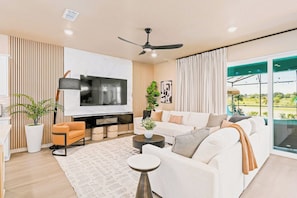 A modern living room with a flat-screen TV, sofa, coffee table, and a ceiling fan.