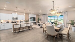 A modern kitchen with a central island, bar stools, and a dining area with a large table and chairs.