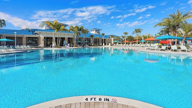 A swimming pool with a 4 ft 6 in depth marker, surrounded by lounge chairs and umbrellas, with a building in the background.