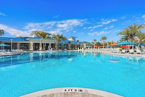 A swimming pool with a 4 ft 6 in depth marker, surrounded by lounge chairs and umbrellas, with a building in the background. - New Resort, Private Pool & Spa, Outdoor Theater, Game Room, Minutes to Disney World (Clermont)