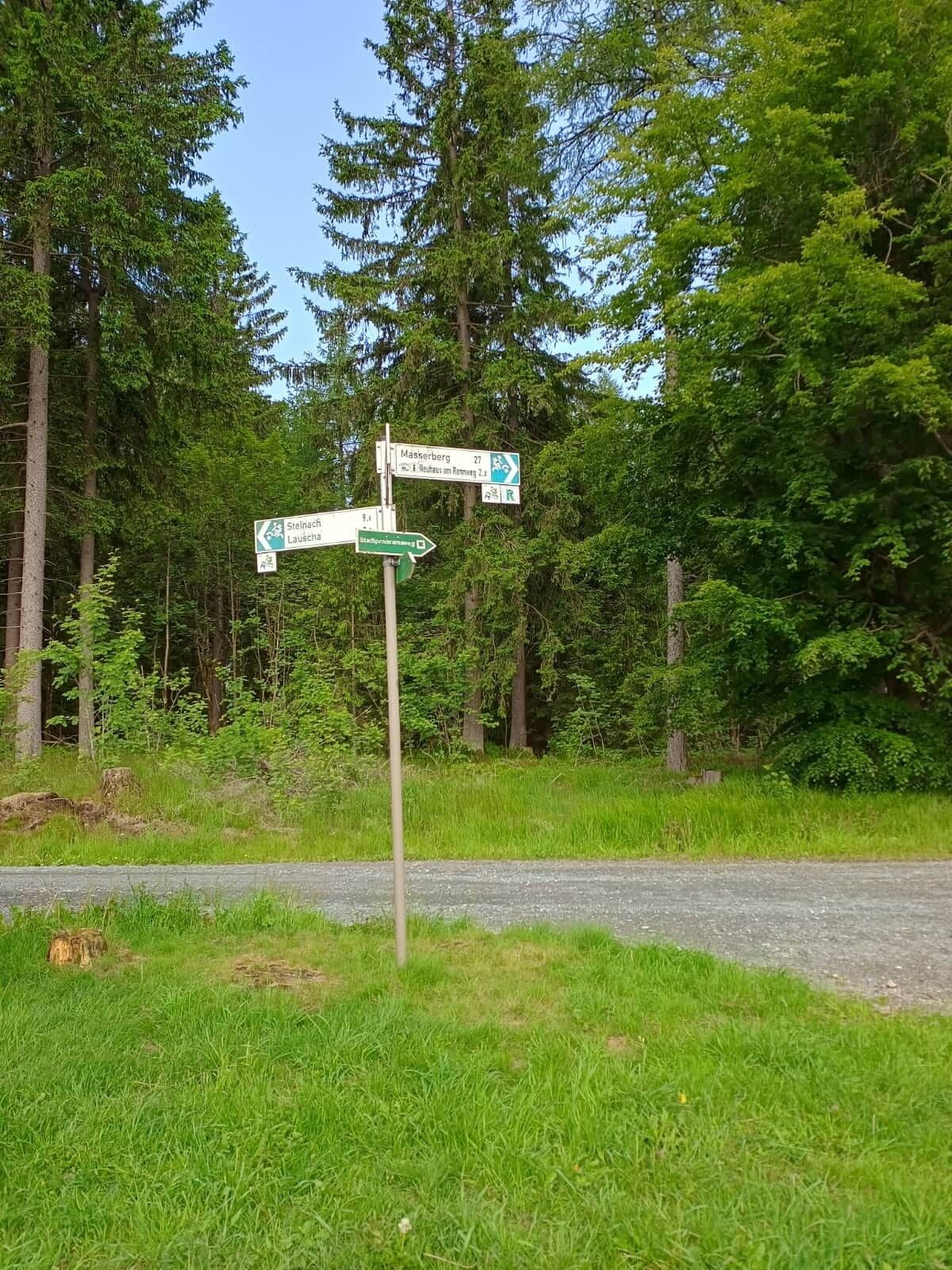 A directional signpost in a forested area with paths leading to Masserberg, Steinach, and Lausch.
