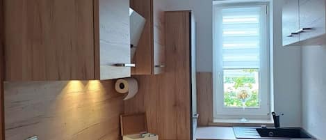 A modern kitchen with wooden cabinetry, a built-in stove, a sink, and a window with a view of greenery.