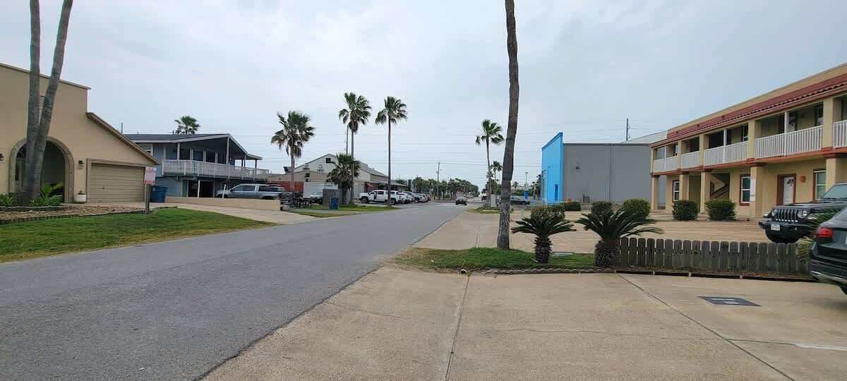 Une vue de rue avec un motel à deux étages, des palmiers et des voitures garées.