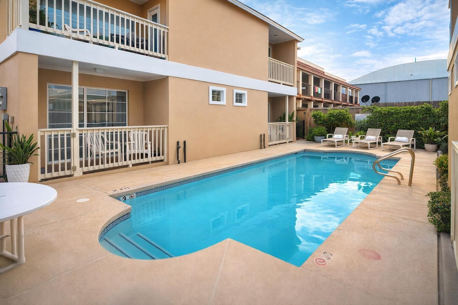 Une piscine avec une terrasse blanche, des chaises longues et un bâtiment doté de balcons.